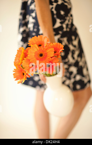 Close up portrait of woman in dress transportant gerber daisies in vase orange Banque D'Images