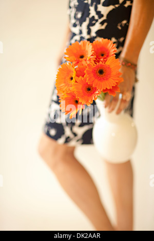 Close up portrait of woman in dress transportant gerber daisies in vase orange Banque D'Images