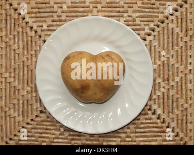 La pomme de terre en forme de coeur organiques sur une plaque sur un tapis tissé. Aimez votre nourriture. Banque D'Images