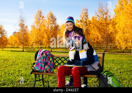 Les enfants, deux garçons fille couvre le visage avec les paumes et rire faire une surprise, guy assis sur le banc du parc en automne Banque D'Images