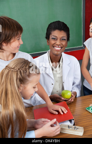 Teacher Holding Apple avec Students Standing At Desk Banque D'Images