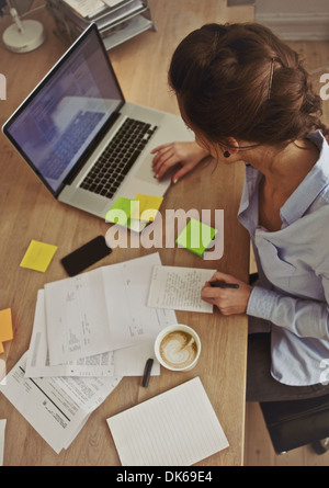 Vue de dessus de jeune femme brune à l'aide d'ordinateur portable au travail. Man à son bureau. Banque D'Images