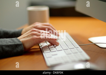 Les mains de la saisie sur le clavier d'un ordinateur travaillant dans son bureau. Banque D'Images