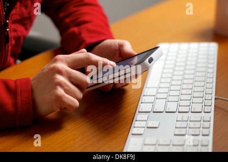 Les mains de la saisie sur un téléphone intelligent écran tactile, travaillant dans son bureau. Banque D'Images