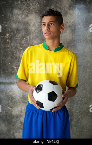 Young Brazilian soccer player en uniforme de l'équipe du Brésil de football contre les couleurs est titulaire d'une favela wall Banque D'Images