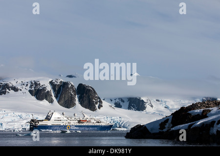 L'Antarctique, l'Île Petermann, navire de croisière ancré près de glacier des montagnes près de Lemaire Channel sur soirée ensoleillée Banque D'Images