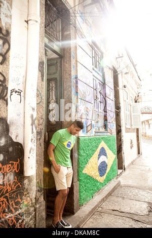 Jeune homme portant le Brésil haut standing in doorway à côté du drapeau du Brésil Banque D'Images