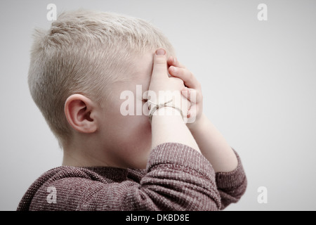 Portrait of boy wearing brown cavalier, couvrant le visage avec les mains Banque D'Images