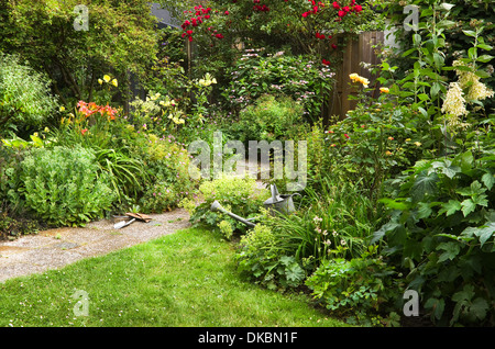 Arrosoir et outils de jardin en fleurs pour le nettoyage sur le jardin de style cottage matin d'été - horizontal Banque D'Images