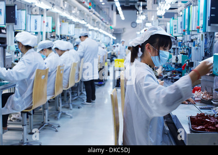 Groupe de travailleurs à l'usine de fabrication de petites pièces en Chine, portant des vêtements, des chapeaux et des masques Banque D'Images