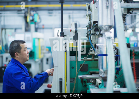 Travailleur de l'usine de fabrication de petites pièces en Chine, appuyant sur le bouton du panneau de contrôle. Banque D'Images
