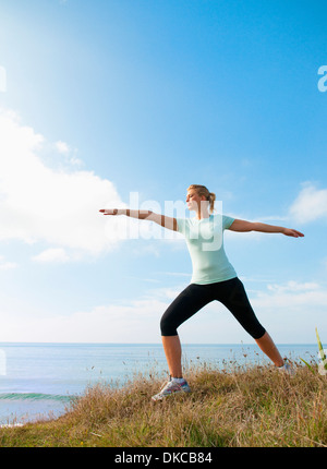 Mid adult woman stretching sur falaise, Thurlestone, Devon, UK Banque D'Images