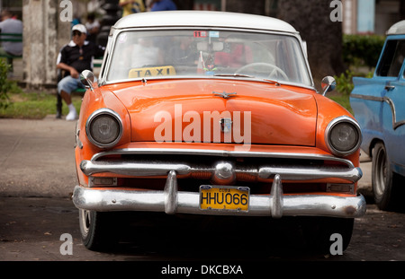 Vieille voiture américaine orange utilisé comme un taxi, avec un chauffeur de taxi assis dans l'arrière-plan, La Havane, Cuba, Caraïbes Banque D'Images