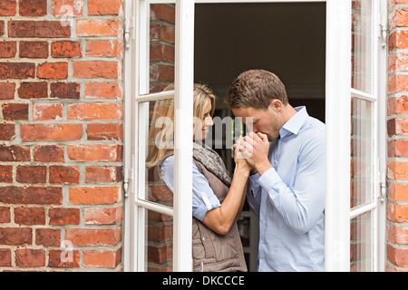 Couple par fenêtre, man kissing woman's hands Banque D'Images