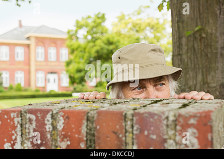 Senior man wearing hat peering over garden wall Banque D'Images