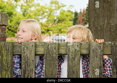 Frère et sœur peering over porte en bois Banque D'Images