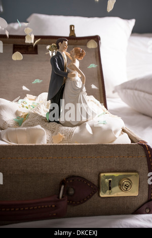 Valise ouverte sur le lit avec des figurines de mariage et confettis Banque D'Images