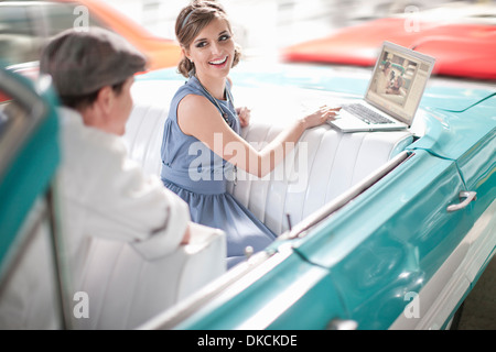 Homme Femme regardant utiliser laptop in back seat of convertible Banque D'Images