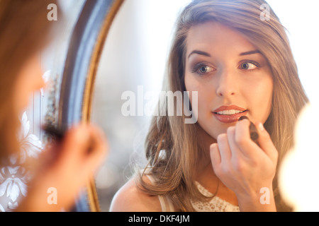Young woman applying lipstick in mirror Banque D'Images
