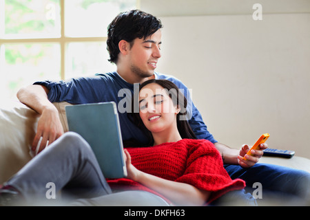 Jeune couple avec tablette numérique et mobile sur le sofa du salon Banque D'Images