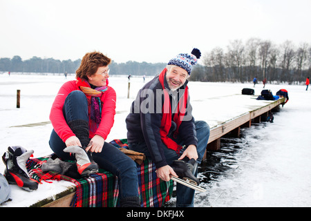 Couple sitting on pier mettre sur patins à glace Banque D'Images