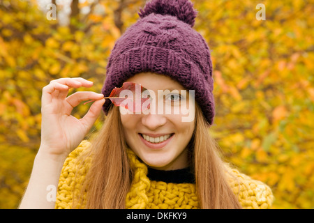 Close up of young woman in park holding autumn leaf sur son œil Banque D'Images