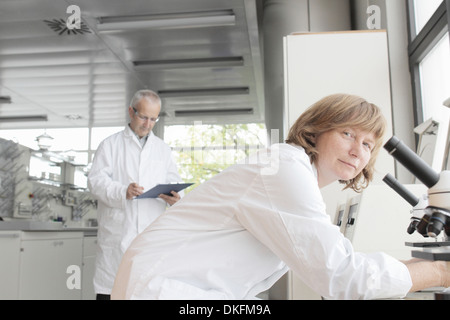 Les scientifiques qui travaillent en laboratoire, femme avec microscope et l'homme en prenant des notes Banque D'Images