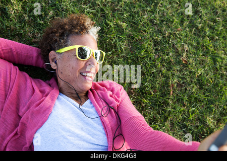 Portrait of senior woman lying on grass wearing sunglasses Banque D'Images