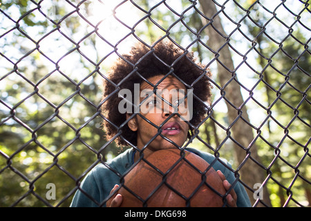 Portrait of young man holding basketball par wire fence Banque D'Images