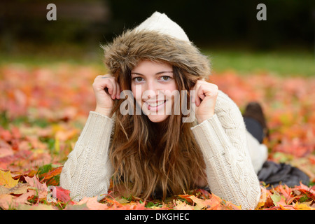 Souriante jeune femme couchée dans les feuilles d'automne Banque D'Images