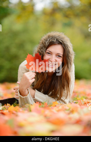 Souriante jeune femme couchée dans les feuilles d'automne Banque D'Images