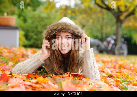 Souriante jeune femme couchée dans les feuilles d'automne Banque D'Images