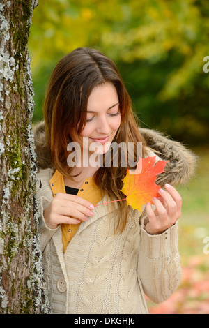 Smiling young woman holding autumn leaf Banque D'Images