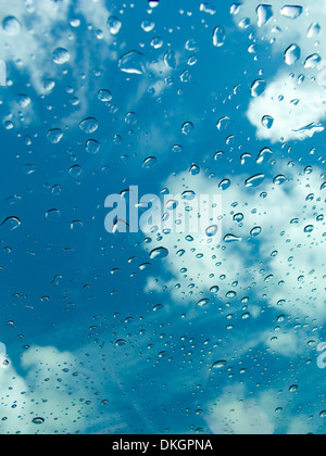 Gouttes de pluie sur le verre clair de panneau de toit ouvrant voiture contre fond de ciel bleu et nuages blancs Banque D'Images