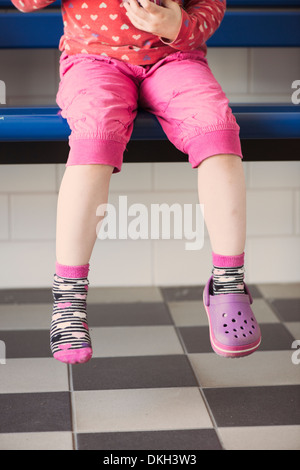 Jeune fille portant une seule chaussure assise seule sur un banc Banque D'Images