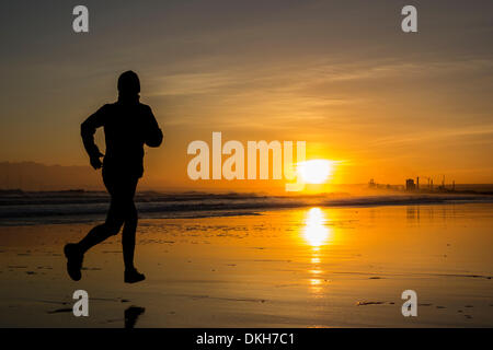 Jogger sur Seaton Carew beach au lever du soleil en hiver. Distance à l'aciérie Redcar. Seaton Carew près de Hartlepool, Angleterre. UK Banque D'Images