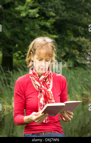 Femme d'âge moyen de la lecture d'un livre dans la nature libre Banque D'Images