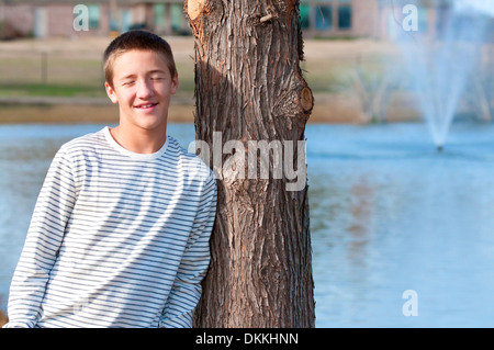 Teen beau avec les yeux fermés s'appuyant sur arbre près d'une fontaine et d'un étang Banque D'Images