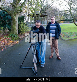 Un professionnel des médias de radiodiffusion directeur vidéo caméraman et avec l'appareil photo sur trépied, tournage dans un parc de la ville, UK Banque D'Images