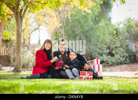 Young Mixed Race Family Enjoying Cadeaux de Noël dans le parc ensemble. Banque D'Images