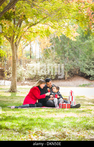 Young Mixed Race Family Enjoying Cadeaux de Noël dans le parc ensemble. Banque D'Images