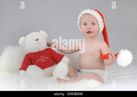 Un bébé portant un chapeau de Père Noël avec son ours de Noël Banque D'Images