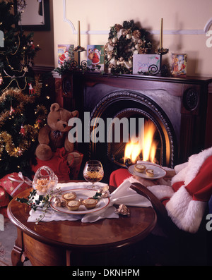 Le père noël, ou santa claus, assise sur un fauteuil à côté d'un feu, de manger de petits pâtés, boire de l'eau de vie, avec un arbre décoré et les cadeaux. Banque D'Images