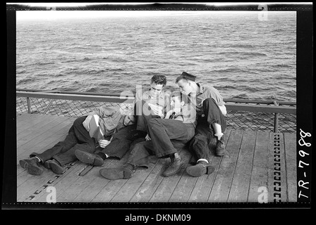 Les hommes enrôlés à bord de l'USS Lexington (CV-16) sont vus en train de lire alors qu'ils sont perchés sur le bord d'un ascenseur, offrant un aperçu franc de la vie quotidienne à bord du porte-avions pendant le service. Banque D'Images