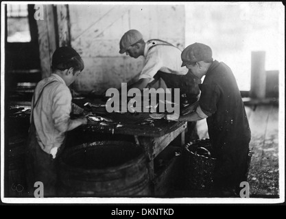 Cette image montre des ouvriers coupant du poisson dans une conserverie de sardine. De grands couteaux tranchants sont utilisés pour traiter le poisson, une étape essentielle pour le préparer à la mise en conserve et à la distribution sur les marchés. Banque D'Images