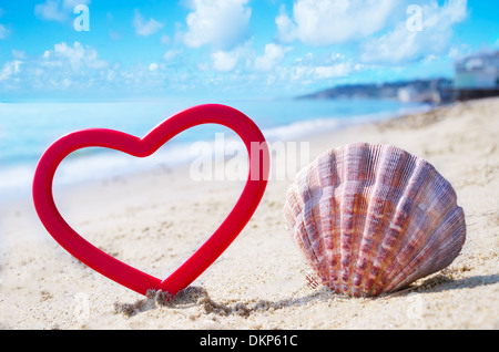 Forme de coeur et d'un coquillage sur une plage de sable à l'océan en journée ensoleillée Banque D'Images