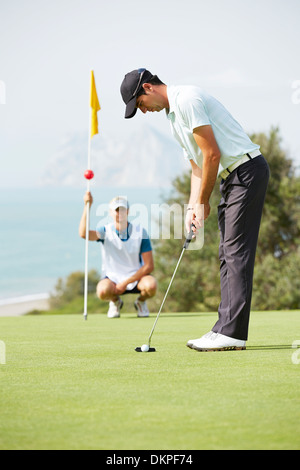 Caddy watching man putt Banque D'Images