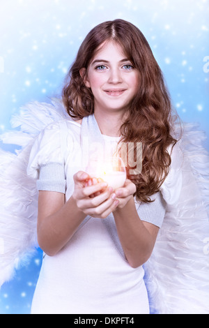 Portrait of sweet angel, belle fille de l'adolescence avec des cheveux bouclés tenant dans les mains une bougie, grande plume des ailes, le temps de Noël Banque D'Images