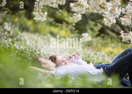 Couple laying in grass en vertu de l'arbre avec des fleurs blanches Banque D'Images