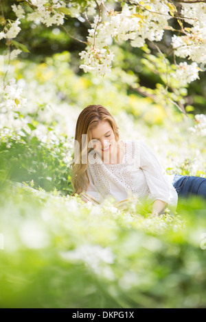 Woman Reading book in grass en vertu de l'arbre avec des fleurs blanches Banque D'Images